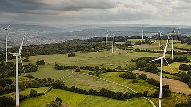 Windkraftanlagen in einer hügeligen Landschaft bei bedecktem Himmel.