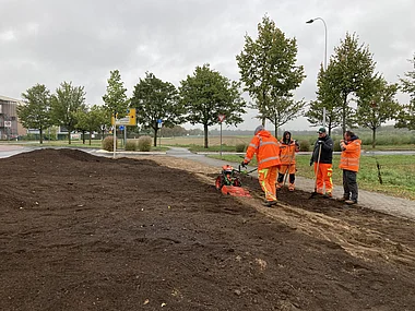 Mitarbeiter pflegen Rasenfläche mit Technik im Freigelände.