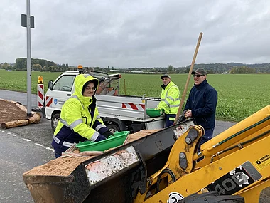 Bauarbeiter entladen Baumstämme mit einem Radlader auf einen Transporter.