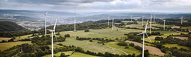 Windräder dominieren eine hügelige Landschaft mit Blick auf eine Stadt.