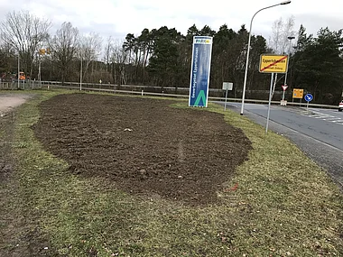 Gewerbegebiet mit Parkplatz und Baumreihen im Hintergrund.