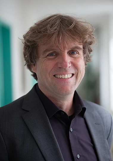 Ein Mann im Anzug lächelt freundlich in die Kamera.