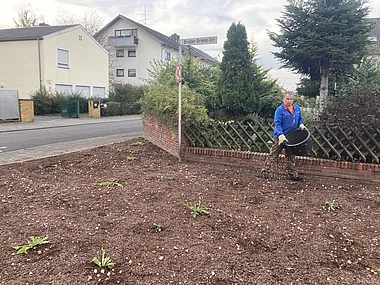 Gärtner jätet Rasen mit Laubbesen neben einem Wohnhaus.