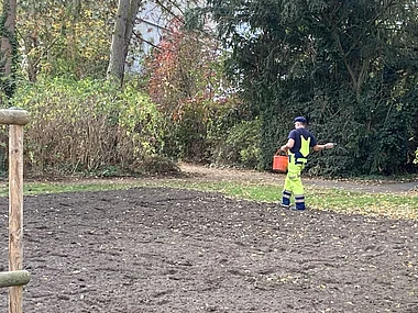 Ein Arbeiter mit gelber Warnweste trägt einen Eimer über einen Feldweg.