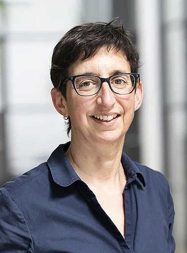 Frau in blauem Hemd, lächelnd vor einem modernen Bürogebäude.