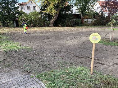 Gärtner mäht Rasen vor einem Wohnhaus mit gepflastertem Weg.
